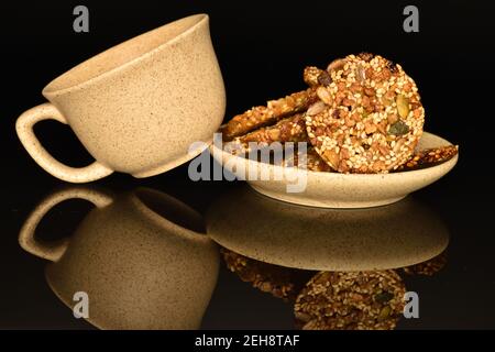 Mehrere ganze frische, duftende, köstliche Walnusskekse, auf einer hellen Keramik-Untertasse, neben einer ist eine Keramik-Tee-Tasse, auf schwarzem Hintergrund. Stockfoto