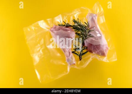 Hähnchenschenkel und Rosmarin im Vakuum verpackt versiegelt für Sous Vide Kochen, isoliert auf gelbem Hintergrund Stockfoto