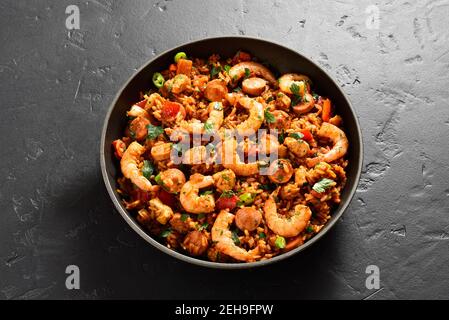 Nahaufnahme des kreolischen Jambalaya mit Garnelen, Hühnerfleisch, geräucherten Würstchen und Gemüse in der Pfanne auf schwarzem Stein Hintergrund. Stockfoto