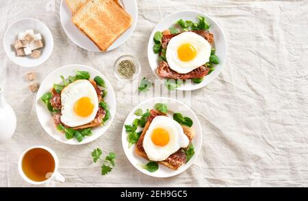 Offene Sandwiches mit Spiegeleiern, Speck und Gemüseblättern auf dem Teller auf hellem Hintergrund. Draufsicht, flach liegend Stockfoto