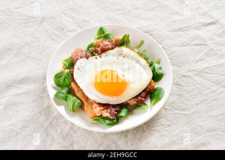 Offene Sandwiches mit Spiegeleiern, Speck und Gemüseblättern auf dem Teller auf hellem Hintergrund. Nahaufnahme Stockfoto