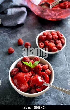 Himbeer-Sorbet, Eisportionierer mit frischen Beeren in Schüssel auf blauem Stein Hintergrund. Leckeres sommerliches kaltes Dessert. Stockfoto