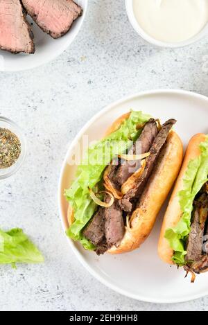 Sandwiches mit Rindfleisch und karamellisierten Zwiebeln auf dem Teller auf hellem Steingrund. Draufsicht, flach liegend, Nahaufnahme Stockfoto