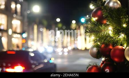Nahaufnahme von festlich geschmückten Outdoor Weihnachtsbaum mit leuchtend roten Kugeln auf verschwommenem funkelnden Feen Hintergrund. Defokused Girlande Lichter, Bokeh eff Stockfoto