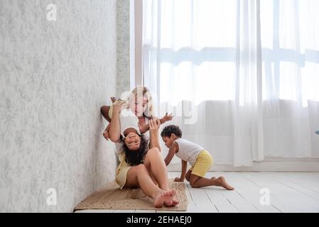 Junge kaukasische blonde Mutter mit afroamerikanischen Sohn und Tochter verbringen Zeit zu Hause zusammen. Viel Spaß, spielen verstecken und suchen, Umarmung, Kuss. Der Tenderne Stockfoto
