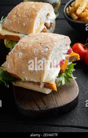 Burger mit Fischfingern frischer Salat, Tomate und Tartarsoße, auf Holzschneidebrett, auf schwarzem Holztischhintergrund Stockfoto