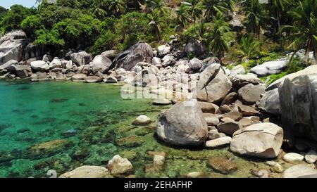 Tropische Palmen und Steine am kleinen Strand. Viele grüne exotische Palmen wachsen an felsigen Küsten in der Nähe von ruhigen blauen Meer in hin Wong Bay an sonnigen Tag in Thailand. Stockfoto