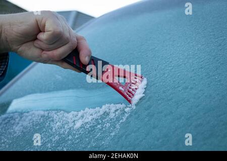 Ein Mann kratzt Eis von einem gefrorenen Windschild oder Bildschirm eines Fahrzeugs an einem kalten Wintermorgen Stockfoto