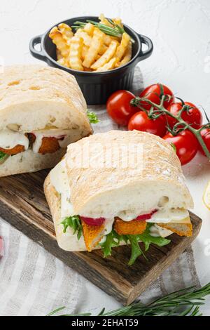 Burger mit Fischstäbchen frischer Salat, Tomate und Tartar-Sauce Set, auf Holzschneidebrett, auf weißem Hintergrund Stockfoto