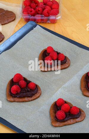 Große gebackene Schokolade Herz hausgemachte Makronen-Kekse mit frischen Himbeeren Auf Pergamentpapier auf einem Backblech Stockfoto