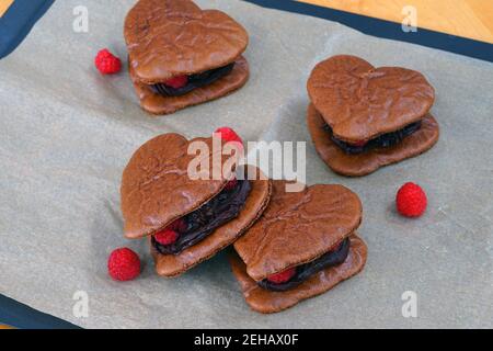 Große gebackene Schokolade Herz hausgemachte Makronen-Kekse mit frischen Himbeeren Auf Pergamentpapier auf einem Backblech Stockfoto