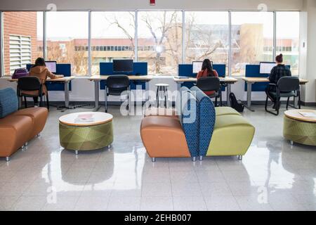 Studentinnen, die an Computerstationen am Fenster arbeiten, zeigen düstere Winterbäume und Gebäude in der Studentenlounge an der Universität Stockfoto