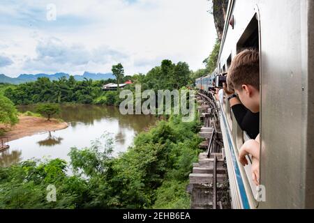Zug rollt über die Holzkonstruktion entlang des Flusses Kwai in Kanchanaburi, Thailand. Auf dem Weg zur berühmten Kwai Brücke. Touristen sehen Stockfoto