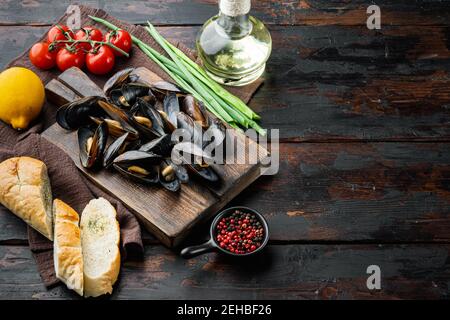 Gekochte Muscheln in Knoblauchsauce mit Petersilie und Zutat, auf Holzschneidebrett, auf altem dunklen Holztisch Hintergrund, mit Copyspace und Platz für Stockfoto