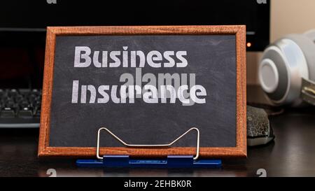 Business Insurance Services Konzept. Der Text ist auf einer Kreidetafel am Arbeitsplatz in der Nähe des Computers geschrieben. Stockfoto
