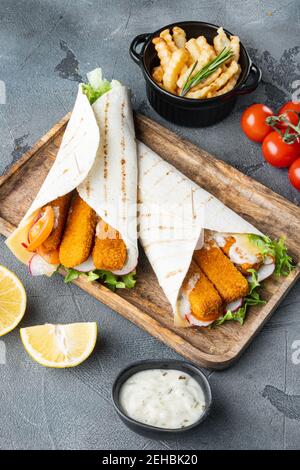 Tortilla-Rolle mit Fischfinger, Käse- und Gemüseset, auf Holzplatte, auf grauem Hintergrund Stockfoto