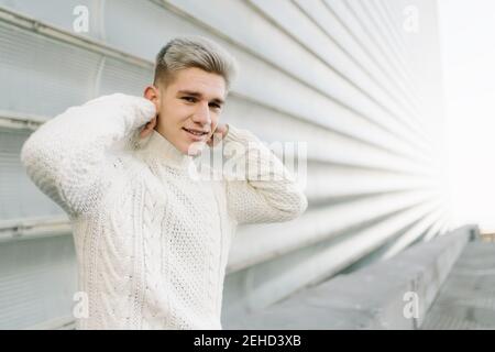 Angenehme, schwanger afroamerikanische Frau in kabellosen Ohrstöpseln mit lockigen Haaren, Textnachrichten auf dem Mobiltelefon in der Nähe des Glasgebäudes Stockfoto