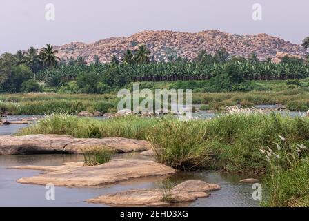 Anegundi, Karnataka, Indien - 9. November 2013: Navabrindavana Insel und Tempel. Tungabhadra Flusslandschaft mit vielen grünen Bäumen und Gras um Stockfoto