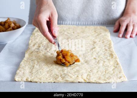 Crop anonyme weibliche Köchin Putting weich gekochten Apfelscheiben auf Teig beim Zubereiten von Gebäck zu Hause Stockfoto