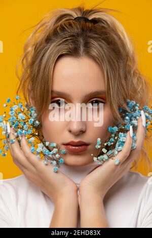 Attraktive junge weibliche stehend mit blauen zarten Gypsophila Blüten auf Das Gesicht auf gelbem Hintergrund im Studio Blick auf die Kamera Stockfoto