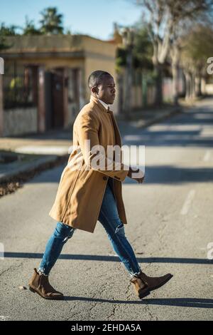 Seitenansicht des selbstbewussten jungen ethnischen männlichen in trendigem Outfit Überqueren der Straße an sonnigen Tag Stockfoto