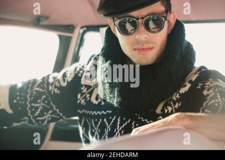 Crop serious männlichen Modell in weich gestrickt Retro Pullover mit Ornament und Kragen ruhen auf Transport an sonnigen Tag Stockfoto