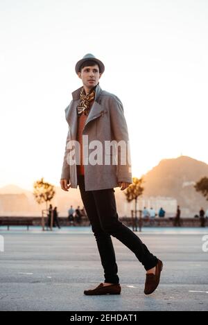 Junge trendige Mann in Hut und Vintage-Kleidung suchen weg Gegen den Berg auf der Straße tagsüber Stockfoto