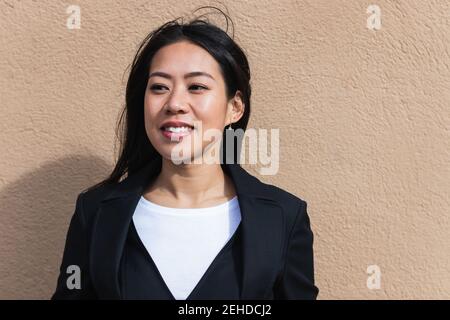 Asiatische Brünette Frau mit langen Haaren an der Wand gelehnt und wegschauen Stockfoto