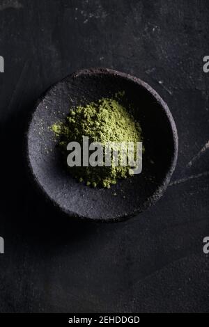 Draufsicht auf pulverförmige grüne Teeblätter in Steinschüssel Platziert auf schwarzem Tisch für Tee und Aroma Stockfoto