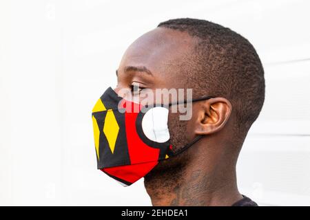 Seitenansicht des jungen afroamerikanischen Mannes, der wegschaut Helle Maske mit Ornament während der Coronavirus-Periode auf hellem Hintergrund Stockfoto