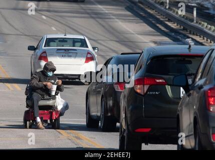 Austin, Texas 19. Feb 2021: Ein nicht identifizierter Mann in einem elektrischen Rollstuhl nimmt Geld in die Abbiegespur einer belebten Straße. Kredit: Bob Daemmrich/Alamy Live Nachrichten Stockfoto