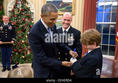 Präsident Barack Obama unterzeichnet die Besetzung von Brayden Myers, 9, bei der Förderung-Zeremonie für Brayden Vater, Military Aide Lieutenant Commander Timothy J. "Tim" Meyers, USN, fördern ihn in den Rang eines Kommandanten im Oval Office, 5. Dezember 2014. Stockfoto