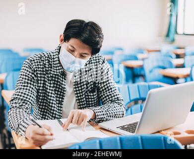 Junge Schüler tragen Gesichtsmaske und studieren im Klassenzimmer Stockfoto