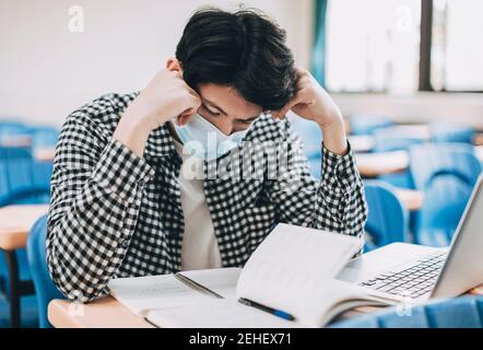 Gestresste junge Schüler tragen Gesichtsmaske und Lernen im Klassenzimmer Stockfoto