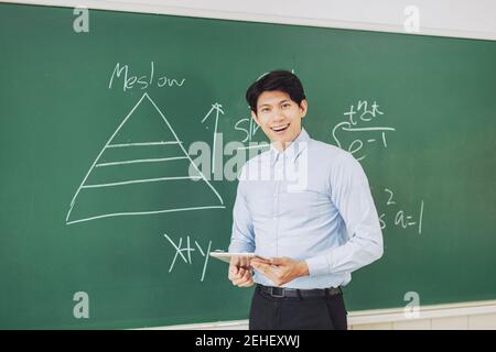 Junge lächelnde Lehrerin, die vor der Tafel steht Stockfoto
