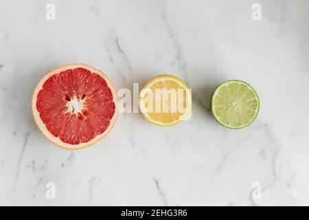 Frische Zitrusfrüchte, Grapefruit, Zitrone und Limette, geschnitten auf einem Marmorhintergrund Stockfoto