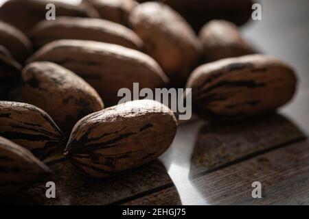 Eine Makroaufnahme mit selektivem Fokus auf eine Handvoll Pekannüsse in Schalen auf einem Holztisch. Stockfoto