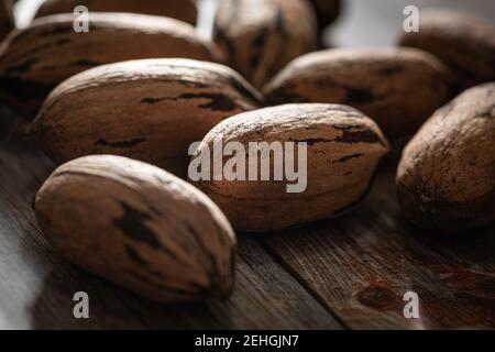 Eine Makroaufnahme mit selektivem Fokus auf eine Handvoll Pekannüsse in Schalen auf einem Holztisch. Stockfoto