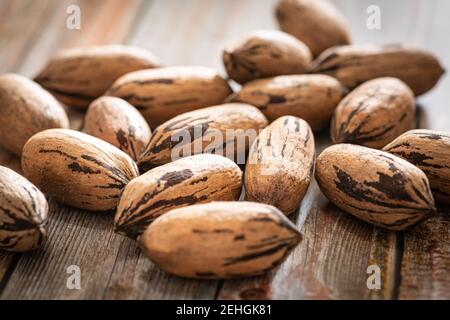 Eine Makroaufnahme mit selektivem Fokus auf eine Handvoll Pekannüsse in Schalen auf einem Holztisch. Stockfoto