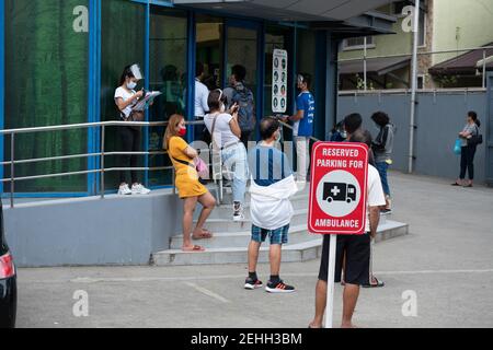 Männer und Frauen warten außerhalb einer Klinik tragen Gesichtsmasken und Schilde auch sozial entfernt, Cebu City, Philippinen Stockfoto