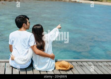 Flitterwochen romantoc Paar umarmt und sitzt auf Holzbrücke und genießt ihren tropischen Urlaub. Liebeskonzept. Stockfoto