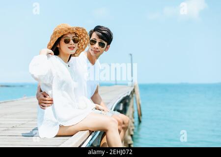 Flitterwochen romantoc Paar umarmt und sitzt auf Holzbrücke und genießt ihren tropischen Urlaub. Liebeskonzept. Stockfoto