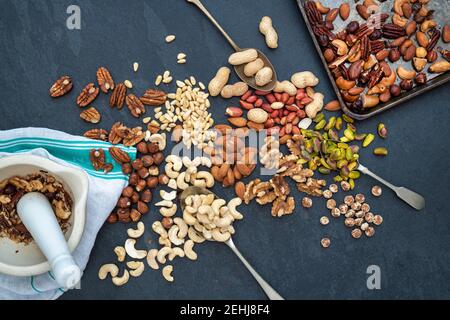 Verschiedene Nüsse mit einem Tablett von gerösteten Nüssen auf einem Schieferhintergrund Stockfoto