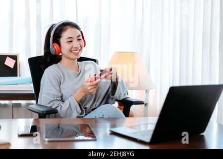 Lustige junge Frau trägt Kopfhörer spielen Computerspiel auf Laptop mit Joypad. Stockfoto