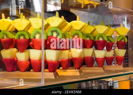 Brocken exotischer Früchte auf Stöcken, Erdbeeren, Birnen, Kiwis und Ananas. Übersichtlich in einer durchsichtigen Glasvitrine dargestellt. Stockfoto