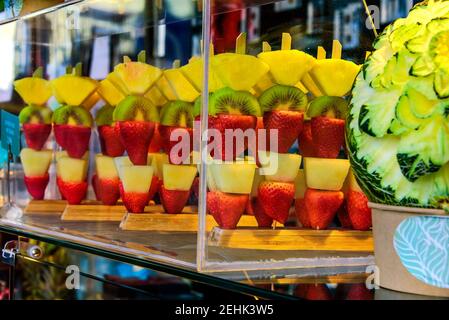 Brocken exotischer Früchte auf Stöcken, Erdbeeren, Birnen, Kiwis und Ananas. Übersichtlich in einer durchsichtigen Glasvitrine dargestellt. Stockfoto