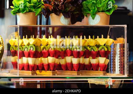 Brocken exotischer Früchte auf Stöcken, Erdbeeren, Birnen, Kiwis und Ananas. Übersichtlich in einer durchsichtigen Glasvitrine dargestellt. Stockfoto
