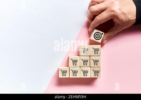 Männliche Hand Platzierung Holzwürfel mit Ziel-Symbol auf der Oberseite der Würfel mit Warenkorb-Icons. Umsatzsteigerung und Erfolg bei der Erreichung des Zielziels i Stockfoto