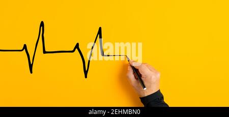 Männliche Hand zeichnet ein Elektrokardiogramm Herzschlagdiagramm auf gelbem Hintergrund. Herz-Gesundheits-und medizinische Check-up-Konzept. Stockfoto