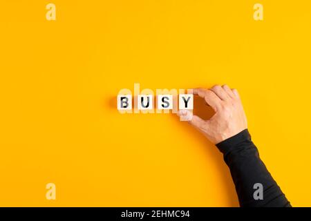 Männliche Hand, die die Holzwürfel mit dem Wort beschäftigt auf gelbem Hintergrund. Überlastung, Stress oder belegtes Konzept. Stockfoto